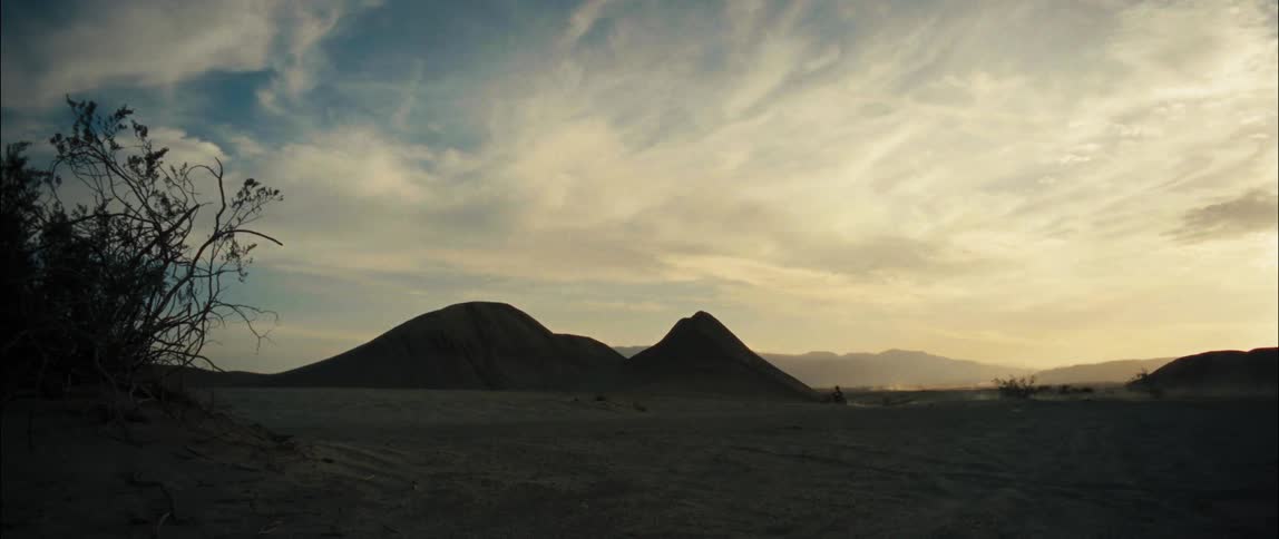 A person rides a bicycle toward sand dunes in the desert