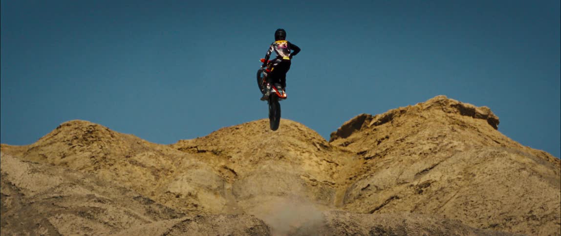 Motorcyclist jumps bike off slope bike and into the air leaving a trail of dust