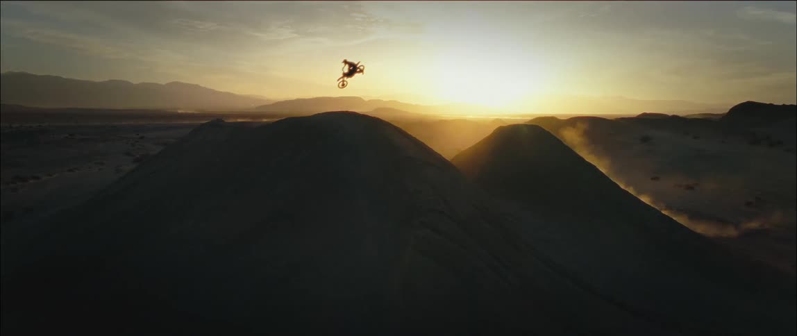 A dirt bike rider leaps through the air and across sand dunes