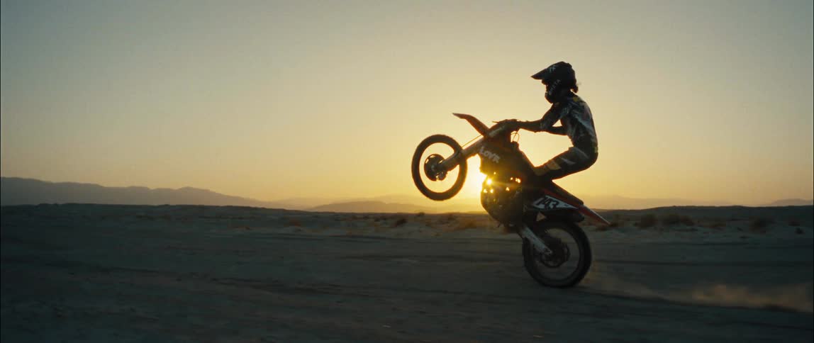 A motorcycle rider does a wheelie while riding through the desert