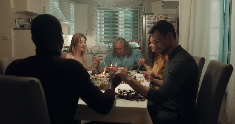 Friends sitting around dinner table in home hold hands to say grace