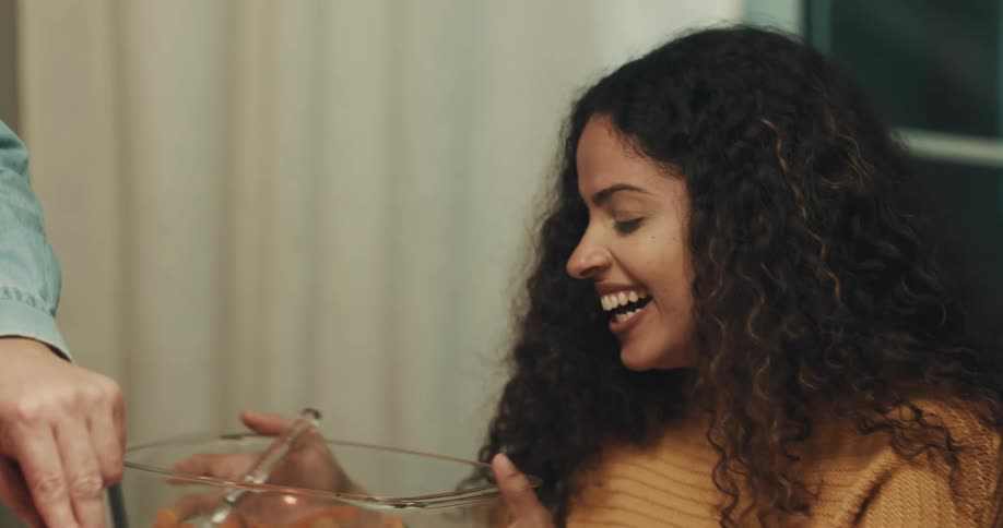 A person slices a piece of meat and places it on a womans plate at a dinner table