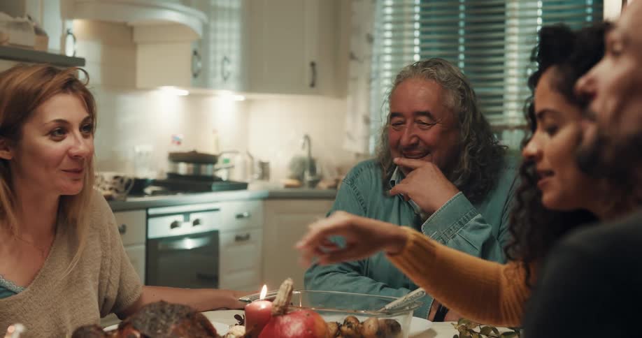 Family and friends talk and laugh while sitting at dinner table