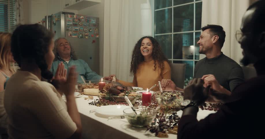 A group of people sitting around a dining table hold hands as grace is said