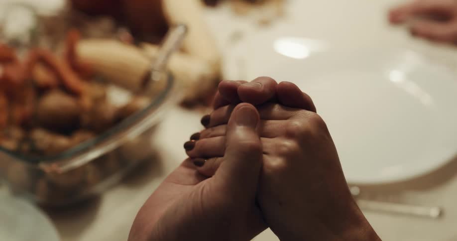 Two people at a table with food and place settings clasp hands