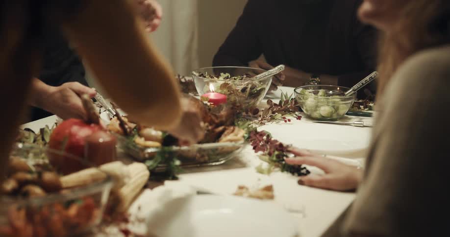 A group of people talk around a dining table as a fried chicked is placed in the center