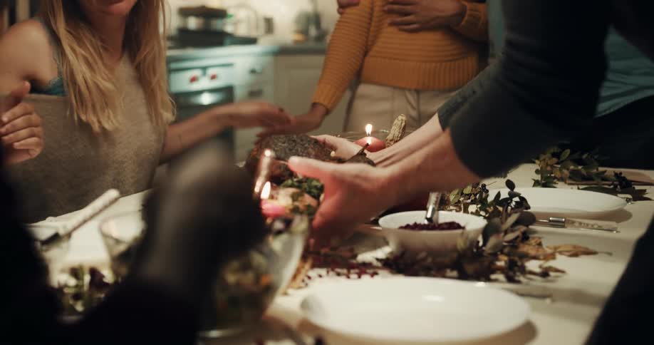 A group of people are sitting at a dining room table and a woman brings the turkey to the table