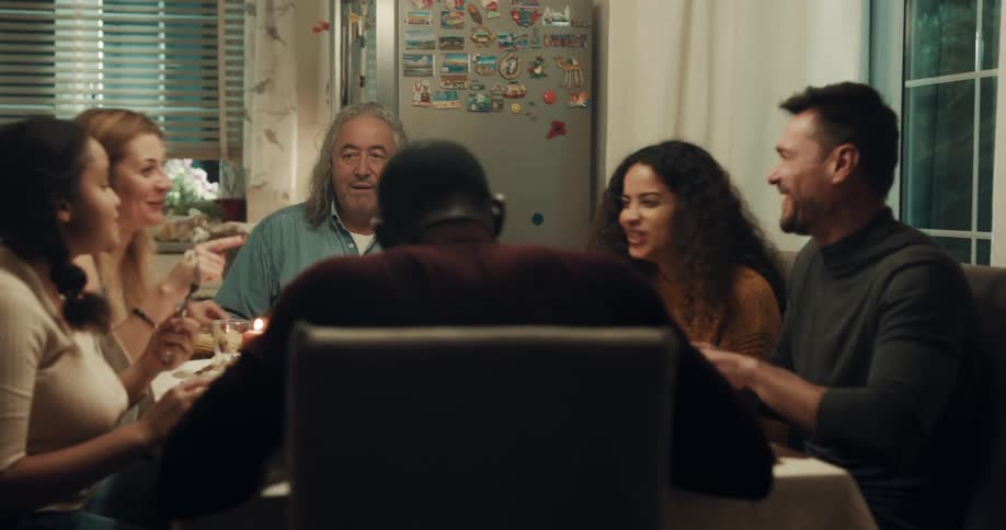 A group of friends and family talk and laugh with eating together at a kitchen table