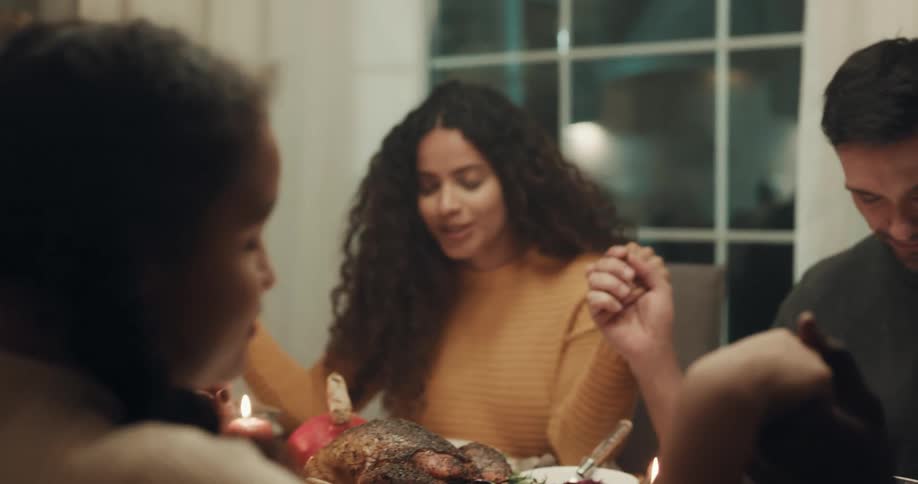 A group of people hold hands as grace is said at a dining table