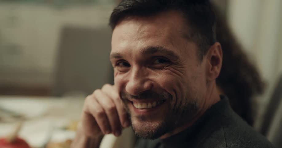 A man is sitting at a table laughing and looking at the camera
