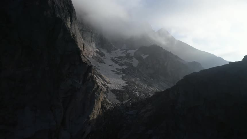 A rock mountain slope covered in patches of snow and mist