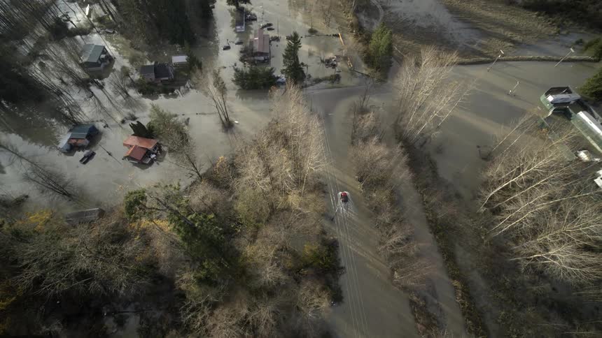 A vehicle travels through the waters of a flooded town during the day