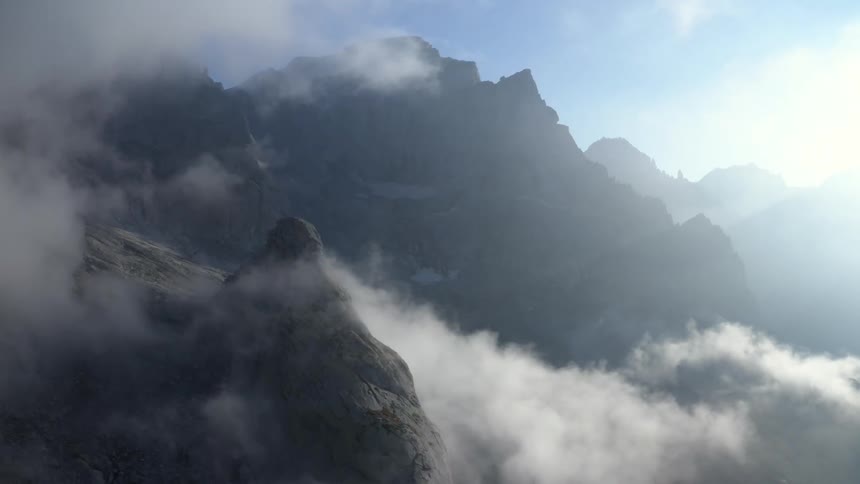 Clouds float around a mountain ridge and peak on a bright sunny day