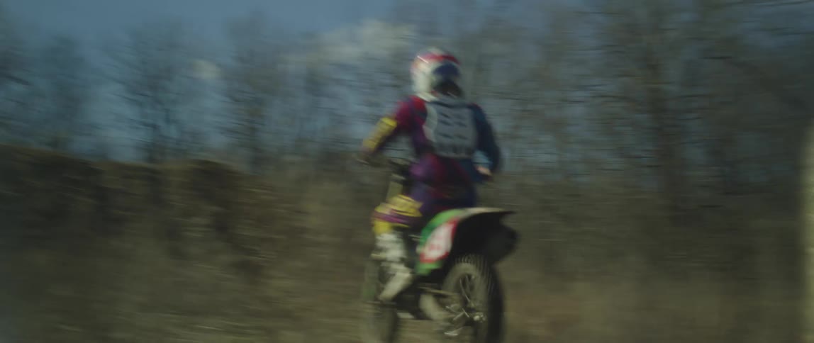 A motorcyclist rides an offroad motorcycle up a dirt ramp and jumps into the air on a clear day