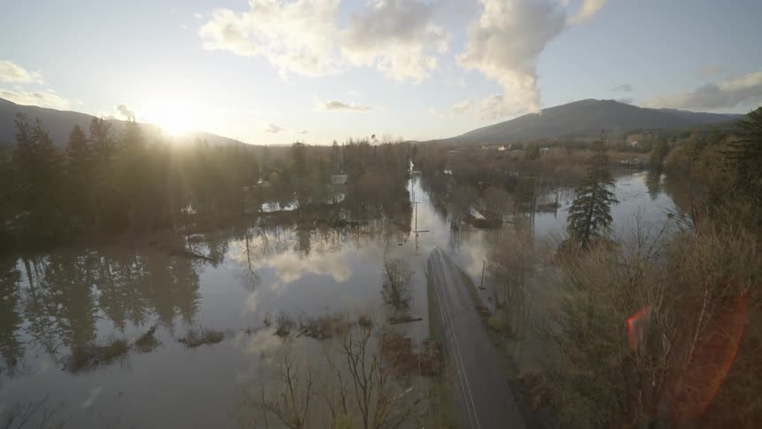 Ascending over a country road to reveal a small town submerged under floodwaters