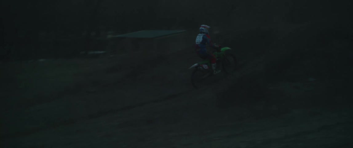 Man riding a dirt bike performing a jump stunt around some trees at dusk