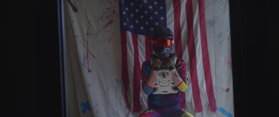Person sitting down in colorful racing gear in front of an american flag