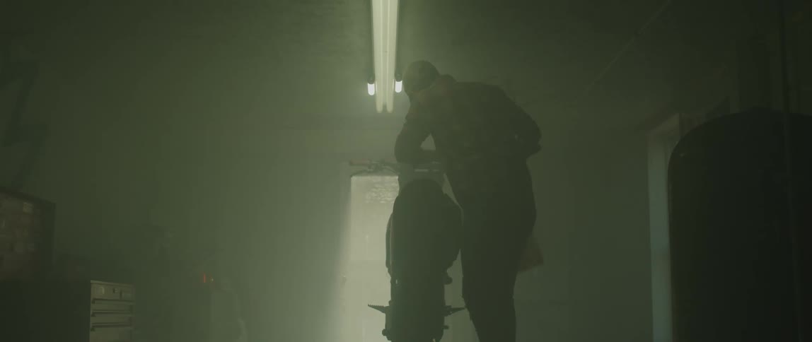 Man carries gas can into dim room to his motorcycle