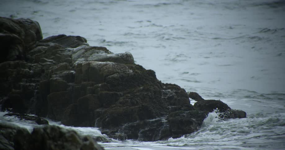 Waves break against a rock formation in the ocean during the day