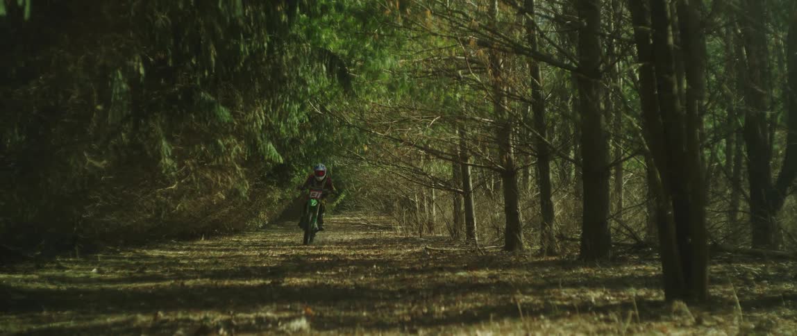 A man rides a motorized dirt bike down a path in a forest