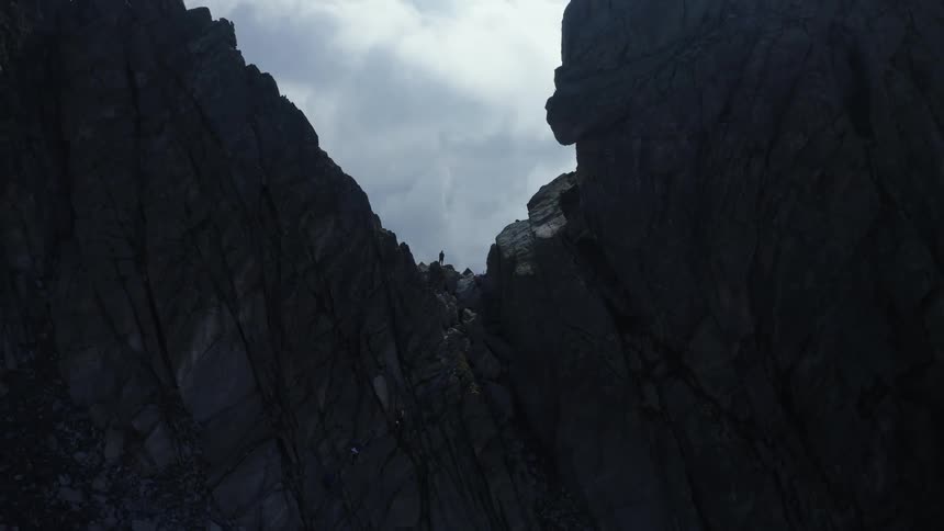 Aerial view of a man standing between the peaks of a mountain top looking at the clouds