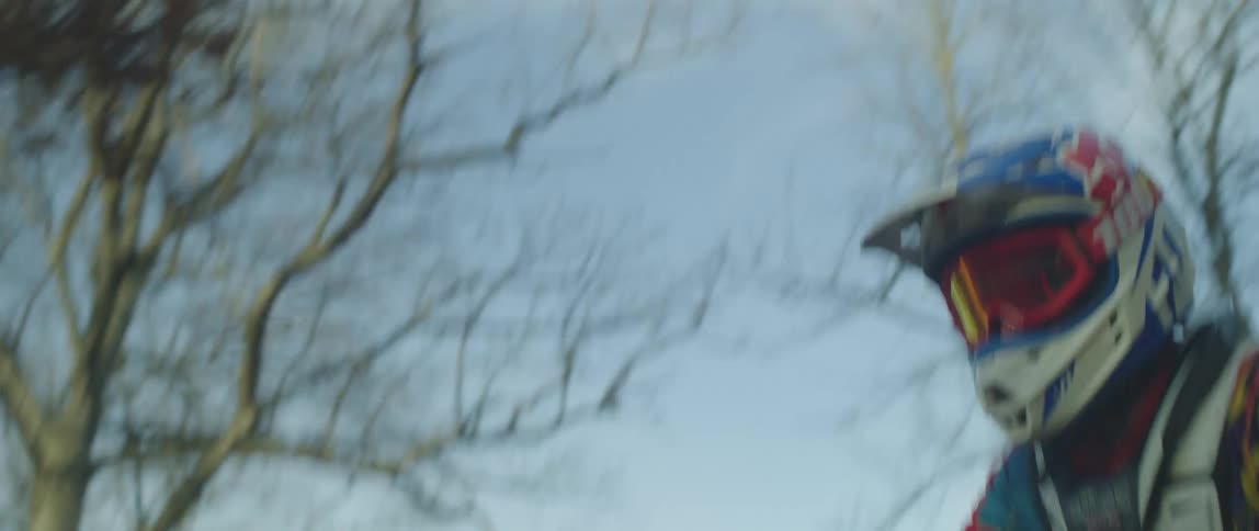 A person rides a dirt bike through the forest during the day