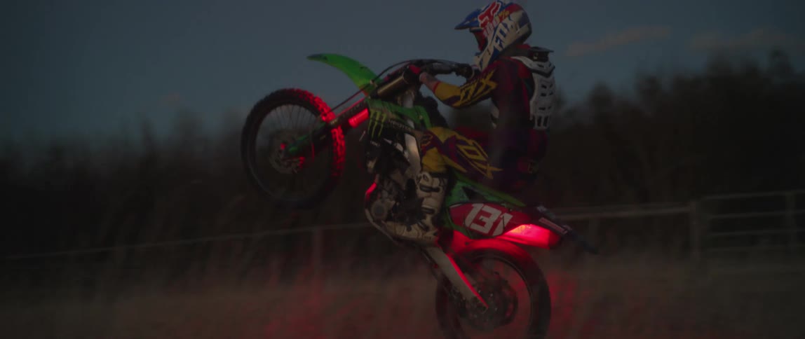 A motorcyclist pops a wheelie on his dirt bike with glowing red lights as he rides through a field