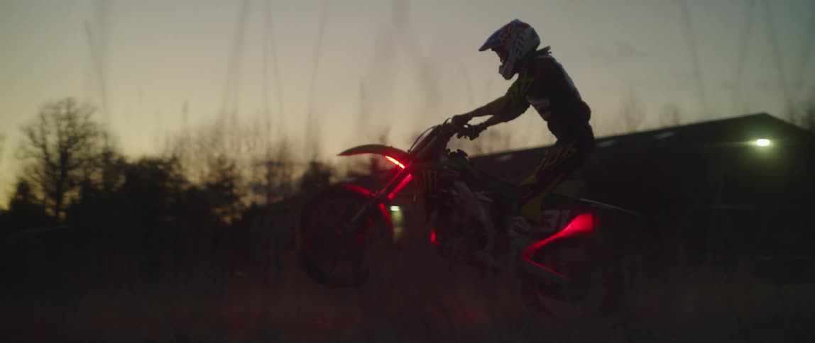 A motocross rider popping a wheelie on a dirt bike with glowing red lights at dusk