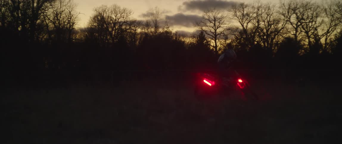 A person is spinning on their dirt bike at sunset with red lights glowing above the wheels