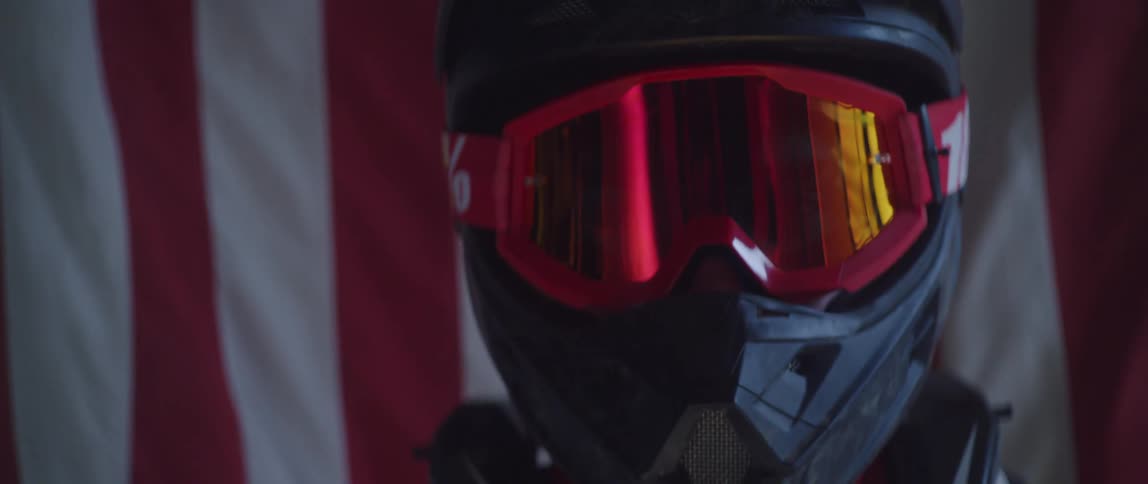 A close up of a person with a helmet and goggles coming into focus with an american flag behind