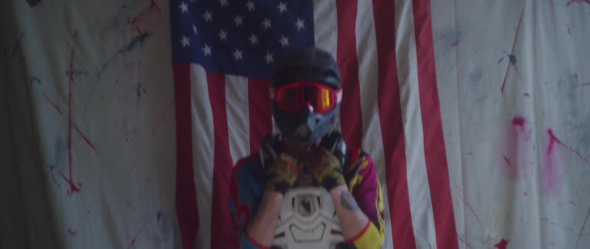 Motorcycle rider wearing helmet and other protective gear sits in front of american flag