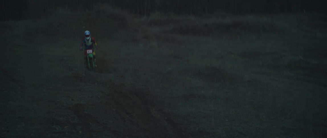 A cyclist on a motorcycle rides down a hill and then leaps across a field