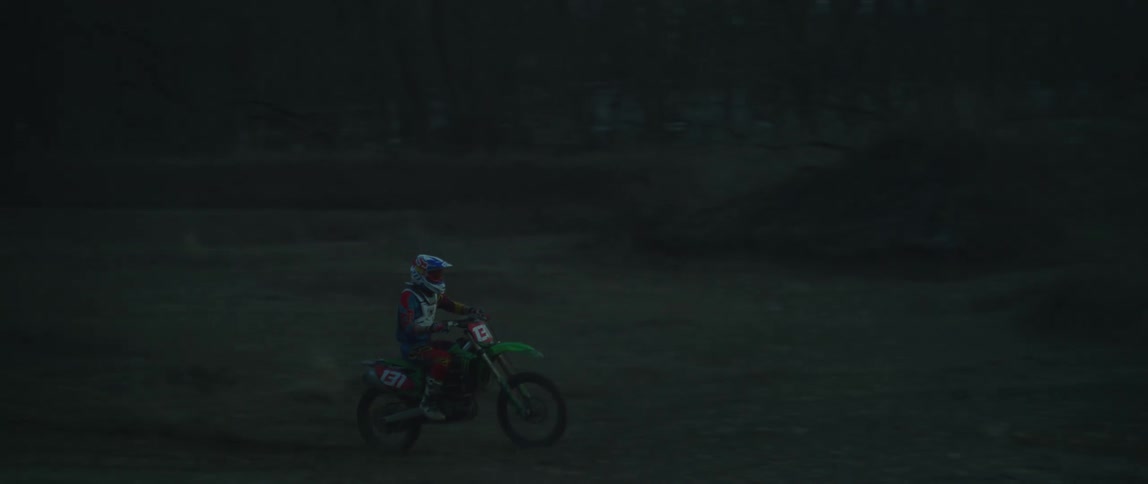 A person riding a dirt bike over berms at sunset
