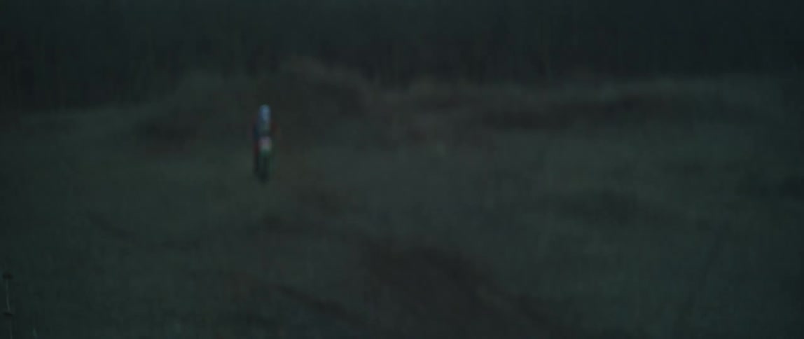 A person is riding a motorcycle through a forest at dusk and performs a jump stunt
