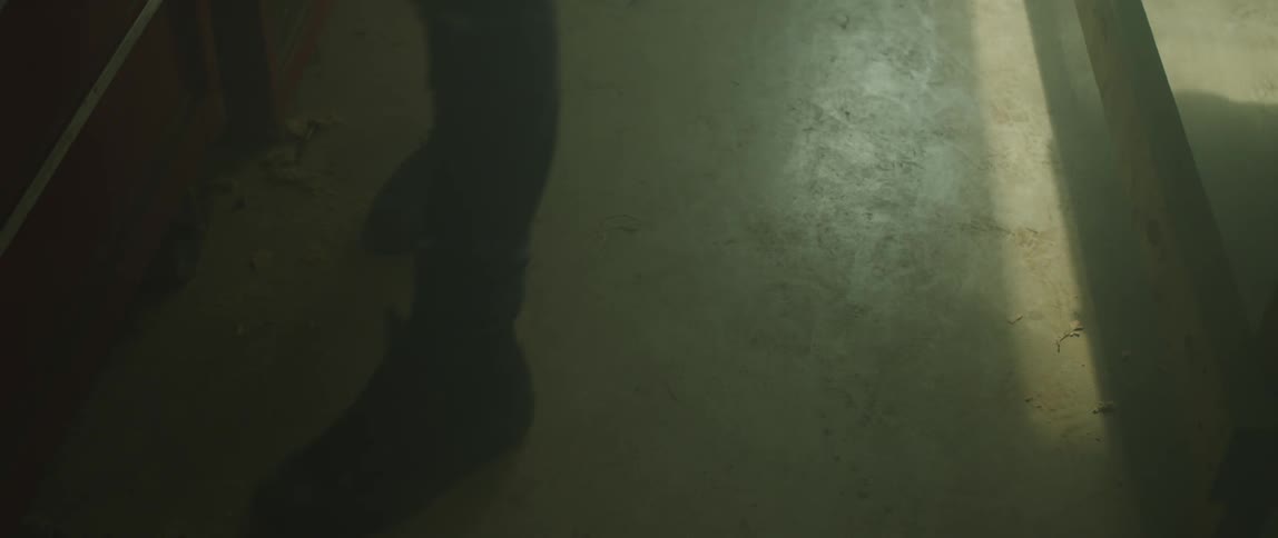 A persons feet are shuffling around in a dimly lit concrete room