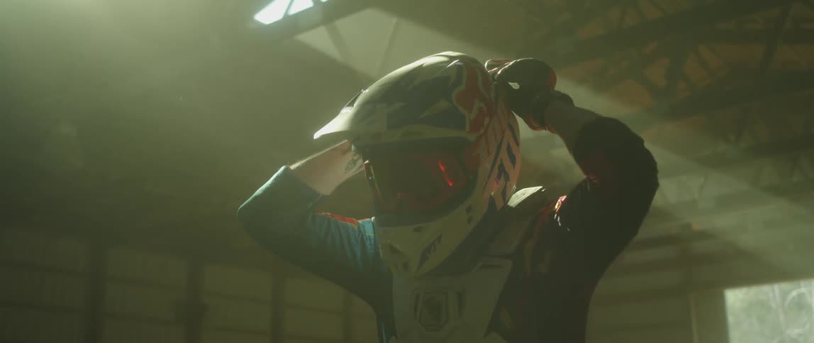 A motocross rider puts on a pair of goggles while inside a garage