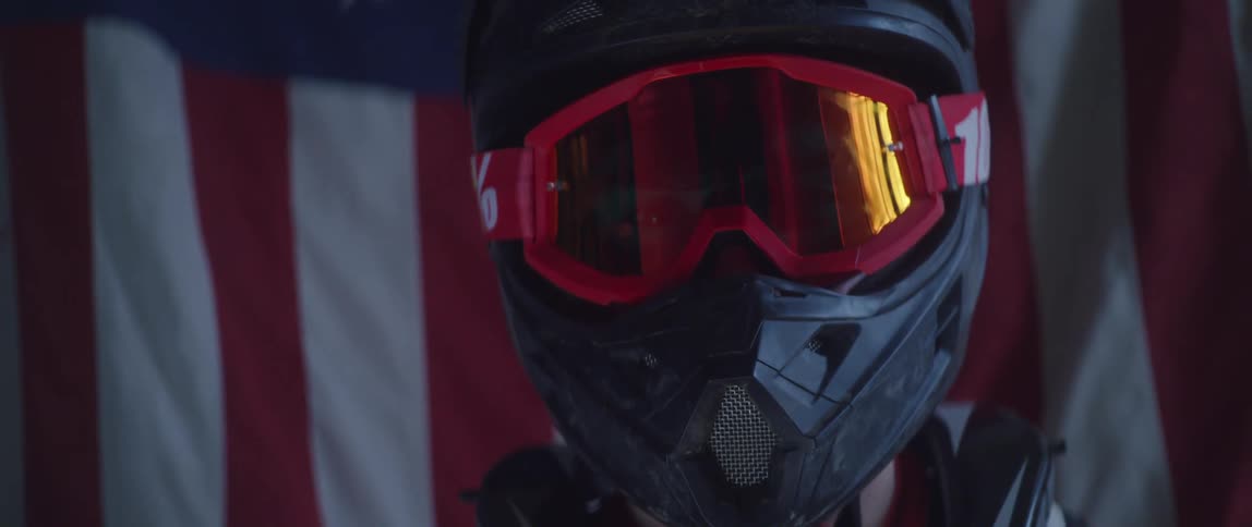 A motocross racer poses in his gear in front of an american flag