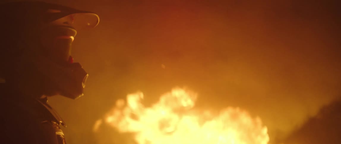 A man in a helmet stands next to a raging fast moving fire