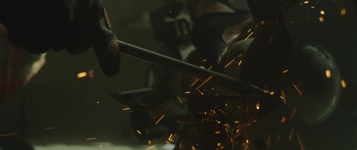 Man wearing a leather glove sharpening a tool on a lathe inside a dimly lit workshop