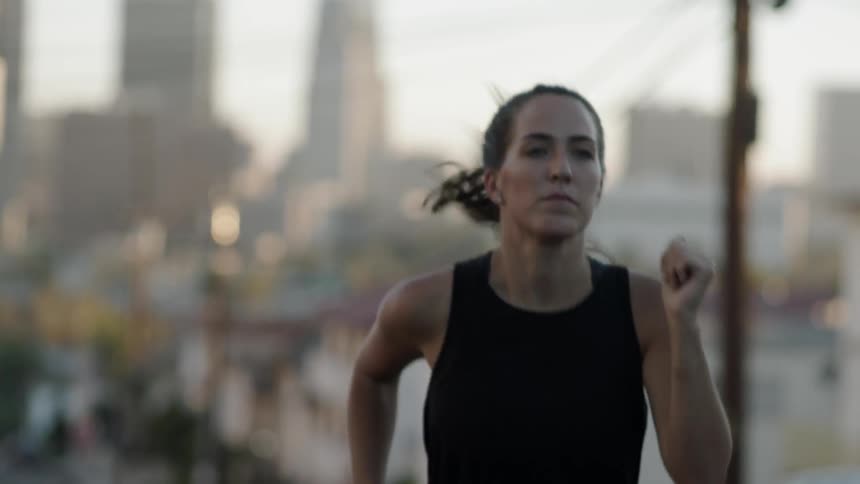 A woman is running outside with a city behind her