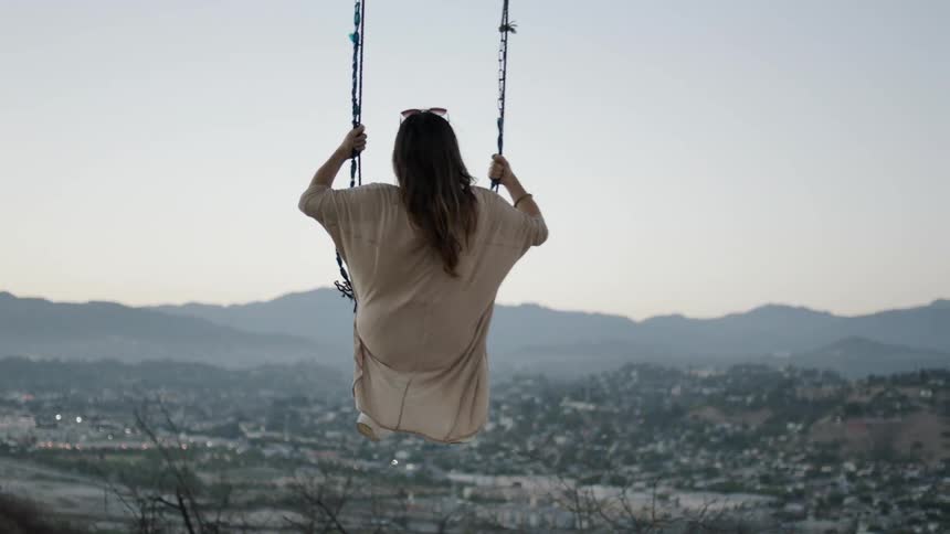 A woman swinging on a hillside above a town