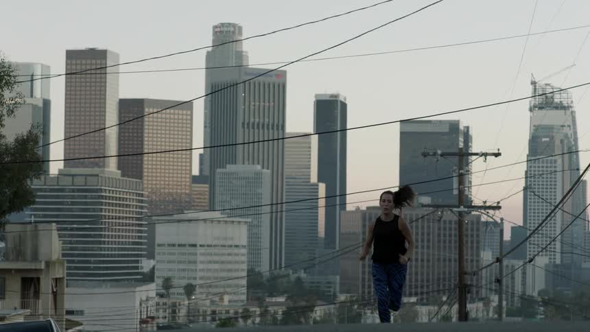 A woman comes running uphill on a street before a city