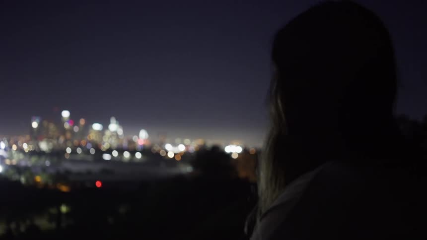 A woman walks up to a view of a city at night