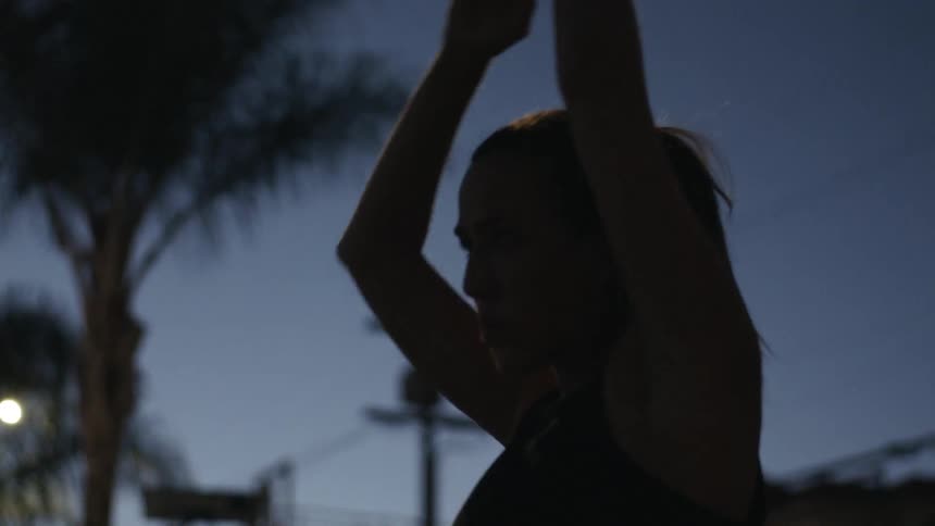 A woman stretches outdoors under a streetlamp