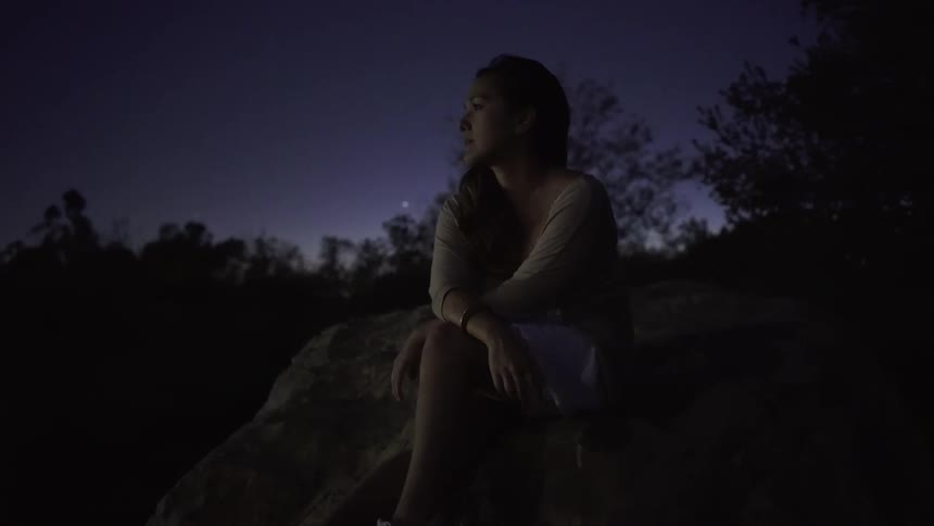 A woman sits with her arms crossed at night looking at a view