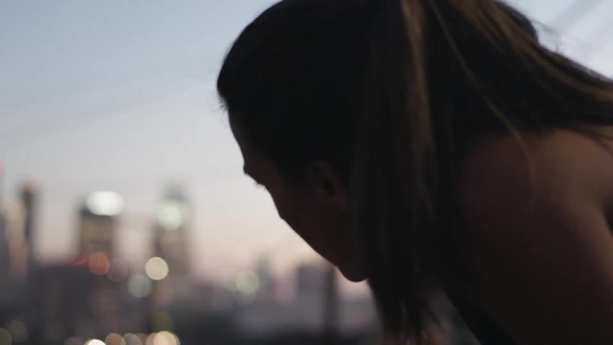 A woman is crouched breathing heavy before a city at sunset