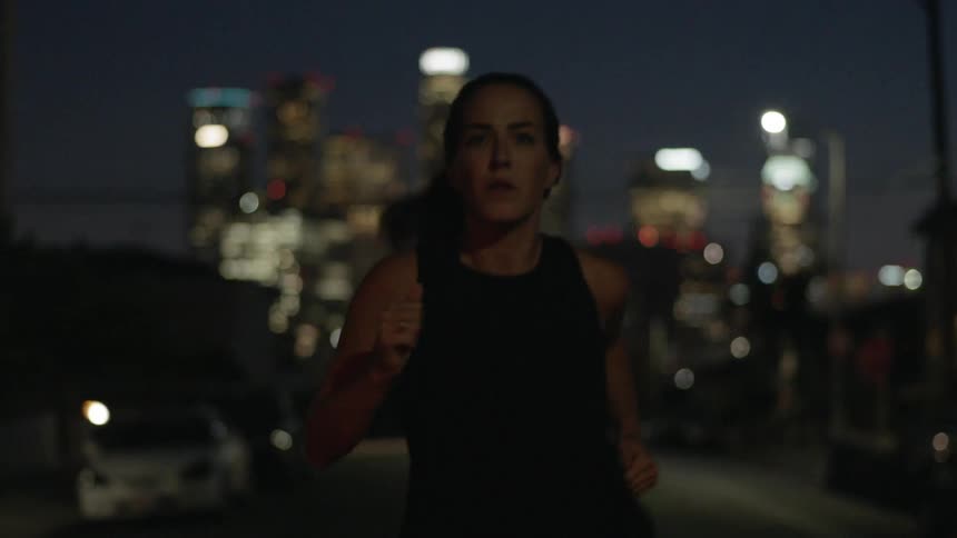 A woman runs outside at night with a lit city behind her