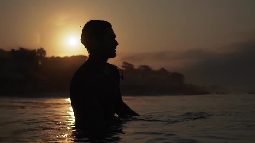 A man is in floating in the water at sunset