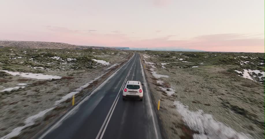 Aerial view of a white car driving on a road in the countryside at sunset