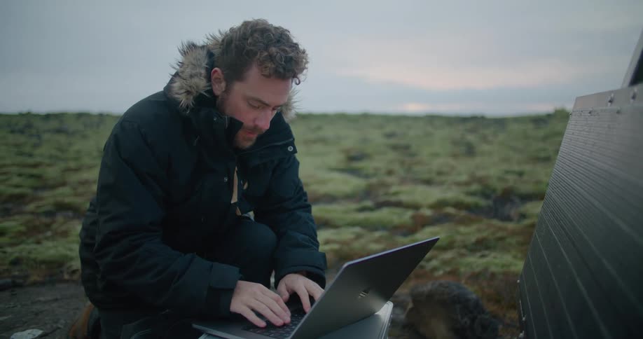 A man types on his laptop and looks at a chart set up in a field